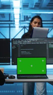 Yüksek teknoloji sunucu merkezinde çalışan çok ırklı mühendisler, verileri analiz etmek için yeşil ekran dizüstü bilgisayar ve bilgisayar kullanıyorlar. Veri merkezindeki altyapıyı krom anahtar kullanarak inceleyen çeşitli çalışanlar