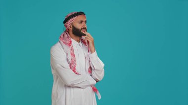 Müslüman kişi düşünceli görünüyor ve yenilikçi çözümler hakkında düşünüyor, ilgileniyormuş gibi yapıyor ve cevap bulmaya çalışıyor. Türbanlı genç adam kamerada düşünceli ve şaşkın görünüyor..