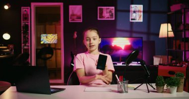 Medya yıldızı çocuk cep telefonunu incelerken kendini videoya çekiyor. Çevrimiçi kanal içeriğini izleyen çocuklar arasında popüler. Neşeli genç kız nüfuzlu cep telefonu özelliklerini sunan video kaydı