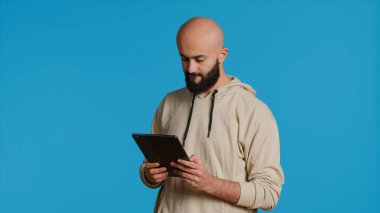 Arap adam internet sitelerine girmek için tablet kullanıyor, internette bir şeyler arıyor ve sosyal medya uygulamaları kullanıyor. Stüdyoda dokunmatik ekran cihazıyla çalışan modern biri. Kamera 1.