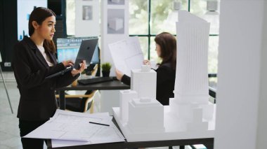 Asyalı müteahhit dizüstü bilgisayarda 3D baskılı model hakkında notlar tutarak, mimarlık bürosundaki maquette 'in ana hatlarını ve ölçeklerini inceliyor. Yeni proje için Cad uzman ölçüm düzeni.