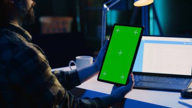 Daire ofisindeki serbest çalışan satış raporlarını analiz etmek ve iş geliştirmeyi planlamak için tablet kullanıyor. Evden çalışan, proje araştırması yapan, izole ekran elektronik aygıtı kullanan adam