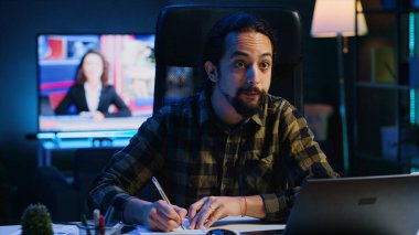 Ofis masasında çalışan uzaktan çalışan, dizüstü bilgisayardan bilgi okuyan ve not defterine yazan biri. Freelancer, telgraf çekerken kalem kullanarak fikirleri kağıda döküyor. Kamera A