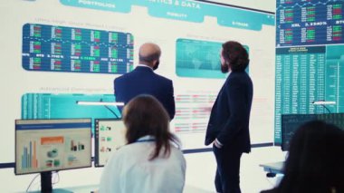 Genel müdür ve CEO, ticari faaliyet durumunu analiz etmek için yıllık bilgi grafiklerini sunan büyük ekrandaki verilerle yeni bir geliştirme stratejisi hakkında görüşlerini paylaşıyorlar. Yatırımcı takımı. Kamera B.