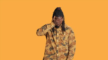 Afro-Amerikalı adam turuncu arka planda duran, görmemek, duymamak ve konuşmamak için sembol gösteren üç bilge maymun işareti gösteriyor. Kamerada ağzını, gözlerini ve kulaklarını kapatan ciddi biri..