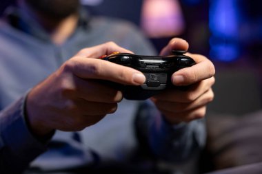 Video oyunları oynarken bulanık arka planda oyuncu tarafından tutulan denetleyiciye odaklan. Oturma odasında TV karşısında oturan bir adamın oyun seansından zevk aldığı oyun alanının yakın plan görüntüsü.