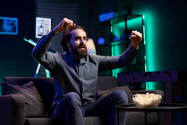 Canlı yayında spor maçı izleyen aşırı sevinçli destekçi, takımın kupayı kazanmasından memnun. Coşkulu bir adam futbol müsabakasına bakıyor, heyecan içinde kollarını kaldırıyor ve golü atıyor.