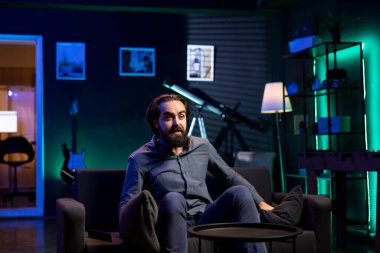 Adam evde oturup televizyon izlemekten zevk alıyor. Şaşırmış bir şekilde. Neon ışıklı apartmandaki kanepede dinlenen izleyiciler televizyon programlarının çarpık dönüşüyle eğleniyor ve hayrete düşüyorlar.