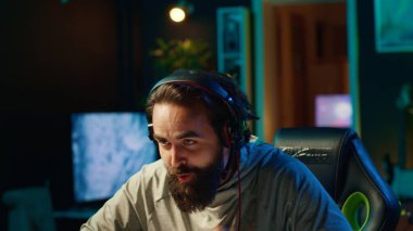 Takım arkadaşlarıyla konuşan neşeli bir oyuncu rekabetçi esport turnuvası oynarken galibiyeti kutluyor. Mutlu adam arkadaşlarıyla çok oyunculu video oyunlarını seviyor, kazandıktan sonra heyecanlanıyor.