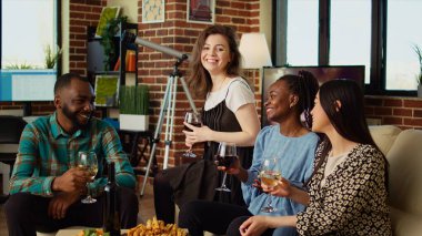 Çok kültürlü arkadaşlar birlikte eğleniyorlar, alkollü içeceklerin ve atıştırmalıkların tadını çıkarıyorlar. Oturma odasında kutlama için bir araya geldiler. BIPOC 'tan bir grup insan evde sohbet ediyor