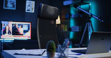 RGB ışıklarıyla aydınlatılan daire. Haber programı yayınlayan akıllı TV 'nin önündeki ofis masası. Laptop, mini ev bitkileri ve kulaklıklar boş odada, kamera B yakın çekim