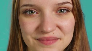 Mavi stüdyo arka planında izole edilmiş neşeli kızın aşırı yakın çekimi. Mutlu, neşeli, gülümseyen bir genç portresi. Yüzünde olumlu bir ifade var.