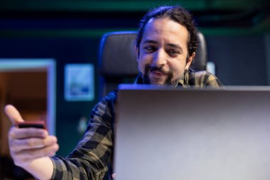 Gülümseyen erkek bankacı dizüstü bilgisayarında internet bankacılığı yapıyor, modern iş ve finansal yönetim eğilimini sergiliyor. Pozitif adam çevrimiçi alımlar için banka kartını kavrıyor.