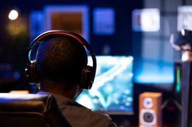 Bulanık arka planda bilgisayar monitörüne video oyunları oynayan, kulaklığa konuşan adama odaklan. Afrika kökenli Amerikalı oyuncu kulaklıkla Esports takımıyla sohbet ediyor.
