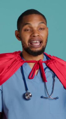 Dikey video hemşiresi süper kahramanı canlandırıyor. Cesaret ve direnç gösteren mücadele hastalıkları, stüdyo arkaplanı. Kostümlü kahraman kılığına girmiş Afro-Amerikan bir doktorun portresi.