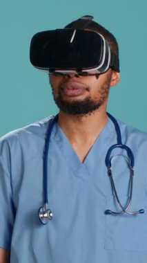 Sanal gerçeklik gözlüğü takan dikey Afrikalı Amerikalı doktor hastayı uzaktan ameliyat ediyor. Hastane personeli yüksek teknolojili video kayıt cihazı kullanıyor, stüdyo arkaplanından izole edilmiş, kamera A