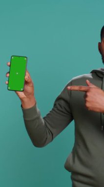 Afro-Amerikan bir adamın dikey video portresi yeşil ekranlı telefon ve stüdyo arka planıyla pazarlama yapıyor. BIPOC çalışanı boş kopya alanı tutuyor. Akıllı telefon aygıtı, kamera B