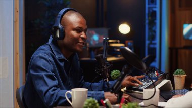 Afrikalı Amerikalı adam podcast kaydediyor, mikrofonu evdeki dinleyiciler için en iyi ses kalitesini ayarlıyor. Profesyonel ses üretme aygıtları kullanan içerik oluşturucu
