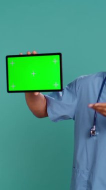 Dikey video neşeli hemşire krom anahtar tabletinde tıbbi talimatlar videosu gösteriyor. Hastane çalışanı yeşil ekran cihazında açıklayıcı sağlık bandı sunuyor, stüdyo arka planı, kamera B