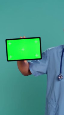 Afro-Amerikan hemşirelerin izole edilmiş tableti işaret eden dikey video portresi. Mutlu hastane personeli elinde krom anahtar dijital cihaz, stüdyo fon, kamera B