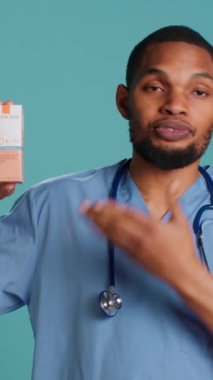 Doktorun yüksek korumalı güneş kremi ürünleri ve stüdyo arkaplanı kullanmanın önemini anlatan dikey video portresi. Afrikalı Amerikalı sağlık uzmanı insanlara ultraviyole ışını kullanmalarını söylüyor.