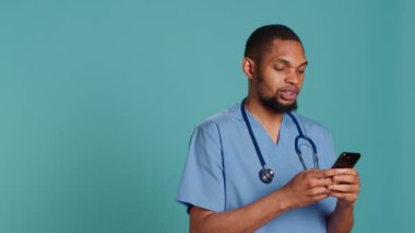 Erkek hemşire hastane mesai molasında sosyal medyayı görüntülemek için cep telefonu kullanıyor. Sağlık görevlisi arkadaşlarına mesaj atmak için akıllı telefonu kullanıyor, stüdyo arkaplanı, kamera A