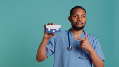 Önlüklü doktor portresi hasta hastalar için ilaç paketi tutuyor. Stüdyoda. Hastane personeli kronik hastalıkları olan hastalar için tablet tavsiye ediyor, kamera A