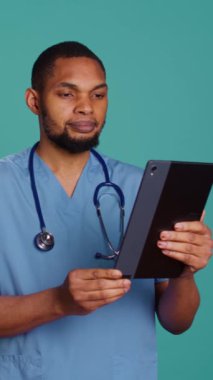 Dikey video görüntülü neşeli doktor, video çağrı toplantısında tablet aygıt kullanarak, tedavi sağlıyor. İnternet teletıp kontrolü sırasında hastaların sorunlarını dinleyen neşeli bir sağlık uzmanı.