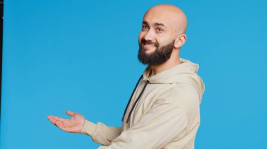 Kameraya bir şeyin reklamını yapan gülümseyen kişi stüdyonun sol ya da sağ tarafını işaret ediyor. Orta Doğulu bir adam pazarlama kampanyası için reklam yapıyor. Kamera 2. El kamerasıyla..