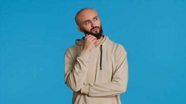 Stüdyoda mavi arka planda durup düşünen düşünceli bir insan. Dalgın Orta Doğulu bir adamın bir konuda kararsız ve şüpheci olması. Kamera 1.