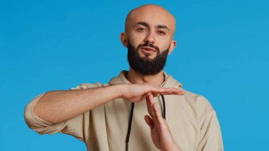 Ortadoğulu kamerada mola jesti yapıyor, mavi arka plan üzerinde çalışmayı bırakmak istiyor. Müslüman yetişkinler bir şeyi durdurmak ya da durdurmak için sembol sunarlar. Kamera 2. El kamerasıyla..