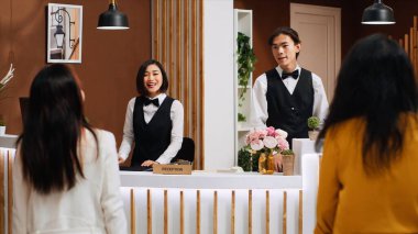 Beş yıldızlı otel resepsiyonuna gelen bir kadın konaklama hakkında resepsiyonistle konuşuyor. Resepsiyon personeli oda rezervasyonunu onaylamak için müşteriye hoş geldin diyor. Üçayak atışı.