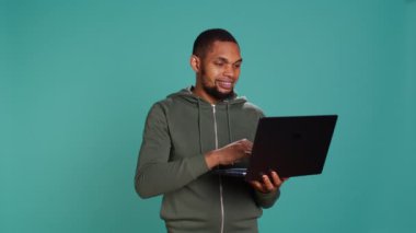 Gülümseyen adam dizüstü bilgisayarda kayıyor, ürünleri ödemek için internet ve kredi kartı kullanıyor. Afrikalı Amerikalı mutlu bir şekilde online alışveriş sitelerine bakıyor, stüdyo arka planında izole edilmiş, kamera B