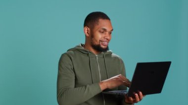 Gülümseyen adam dizüstü bilgisayarda kayıyor, ürünleri ödemek için internet ve kredi kartı kullanıyor. Afrikalı Amerikalı mutlu bir şekilde online alışveriş sitelerine bakıyor, stüdyo arka planında izole edilmiş, kamera A