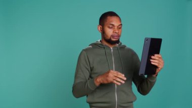 Sinirli bir adam, arkadaşlarıyla video görüşmesi yaparken tablet üzerinde kavga ediyor. Stüdyonun arka planında izole halde. Eşiyle anlaşamayan kaba insan, telekonferans toplantısında küfreden ve işaret eden kişi, kamera B
