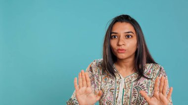 Stern indian woman doing stop hand gesture sign, complaining. Authoritative person doing firm halt sign gesturing, wishing to end concept, isolated over studio background, camera B clipart