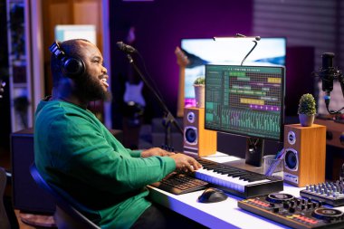 Yeni bir müzik yaratmak için piyano elektronik klavye çalan yetenekli besteci, dijital yazılımda bir şarkı bestelemek için melodileri karıştırıyor. Müzisyen ayarlama ses seviyeleri amfi düğmeleri, midi denetleyici.