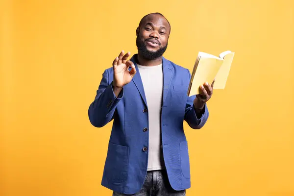 stock image Portrait of jolly african american man recommending interesting book after being entertained by well written story. Joyous person showing positive hand gesturing, enjoying novel, studio background