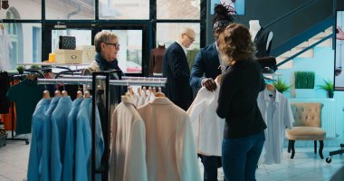 Moda tasarımcısı düzenli müşterilere kıyafet ürünleri öneriyor, mağaza çalışanları yaşlı kadınların indirimli kıyafet almasına yardım ediyor. Alışveriş çılgınlığı sırasında müşterilere yardımcı olan tezgahtarlar. Kamera B.