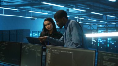 Yardımcı teknisyenler laptop ekranına bakıyor, veri merkezinde çalışıyor, en iyi performansı sağlıyor. Meslektaşlar enerji tüketimini sunucu kulesi bileşenleri üzerinden izleyip beyin fırtınası yapıyorlar.