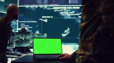 Ordu subayı kontrol odasındaki bir dizüstü bilgisayarda izole edilmiş yeşil ekran görüntüsü üzerinde çalışıyor. Askeri güç üssü personeli federal operasyonlar için uydu dünya haritasını izliyor. Üniformalı komutan. Kamera B.