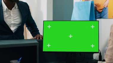 Afrikalı Amerikalı işçiler kasada yeşil ekran ekranlı bilgisayar kullanıyor. Müşteri için bir çantaya giysi koyuyorlar. Çalışan fotokopi ekranını gösteren bilgisayara bakıyor. Kamera A.