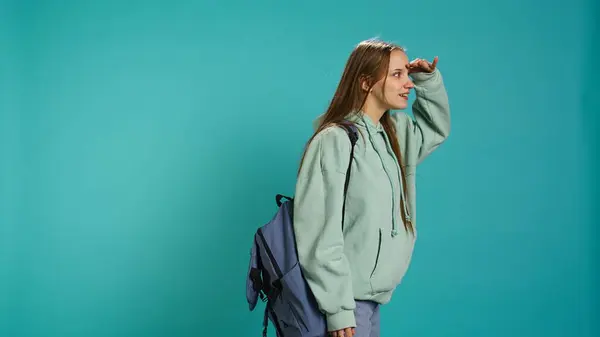 stock image Cheerful voyager student looking around, inviting others to join her, doing hand gesturing. Radiant girl looking in distant horizon, discovering new place with friends, studio background, camera B