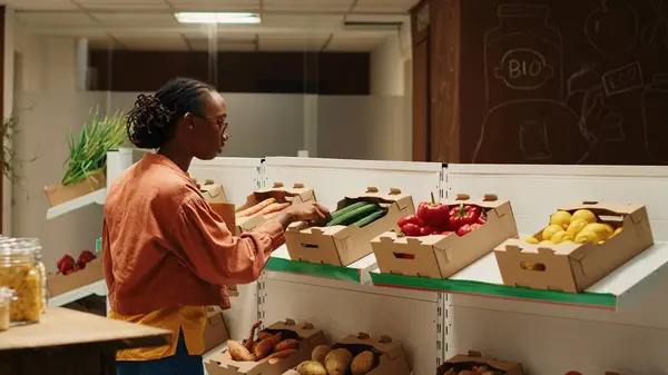 stock image Vegan person searching for freshly harvested vegetables from crates, shopping for natural groceries at local zero waste eco store. African american client looking at organic food items. Camera 1.