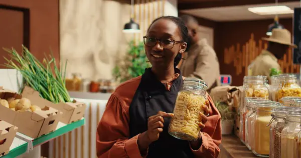 stock image African american vendor presenting variety of pasta in jars, discussing about ethically sourced products and homemade food alternatives. Filming promotional video for healthy lifestyle. Camera 2.