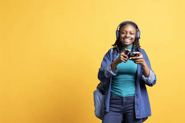 stock image Portrait of happy teenager playing videogames with controller and headphones, studio background. Joyous gamer having fun participating in PvP internet game with joypad, relaxing after school