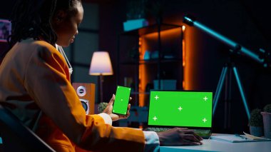 Afrikalı Amerikalı bir kız ekranda aynı izole model şablonu kullanan modern cihazlara bakarak akıllı telefon ve bilgisayar kullanıyor. Genç kadın kopyalama ekranlarını kontrol ediyor. Kamera B.