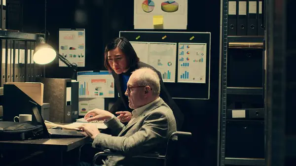 stock image Forensic team examining evidence and medical records to uncover clues, building a profile for the suspect. Law agent helps senior investigator with legal documents, wheelchair user. Camera A.