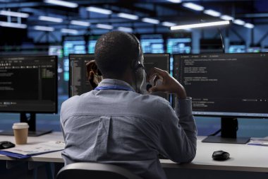 Sunucu odasındaki teknisyen çağrı merkezi görevlerini yönetiyor, birden fazla bilgisayar ekranını izlerken kulaklığa konuşuyor. Çalışan müşterilerle kulaklıkla konuşuyor.