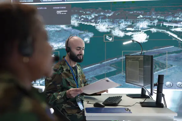 stock image Skilled IT engineer monitoring satellite CCTV footage recorded on computer and big screen in military command post. Army trooper working in the reconnaissance division for information.